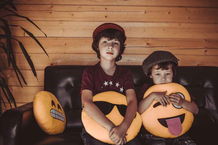 two boys sitting on sofa holding emoji throw pillows